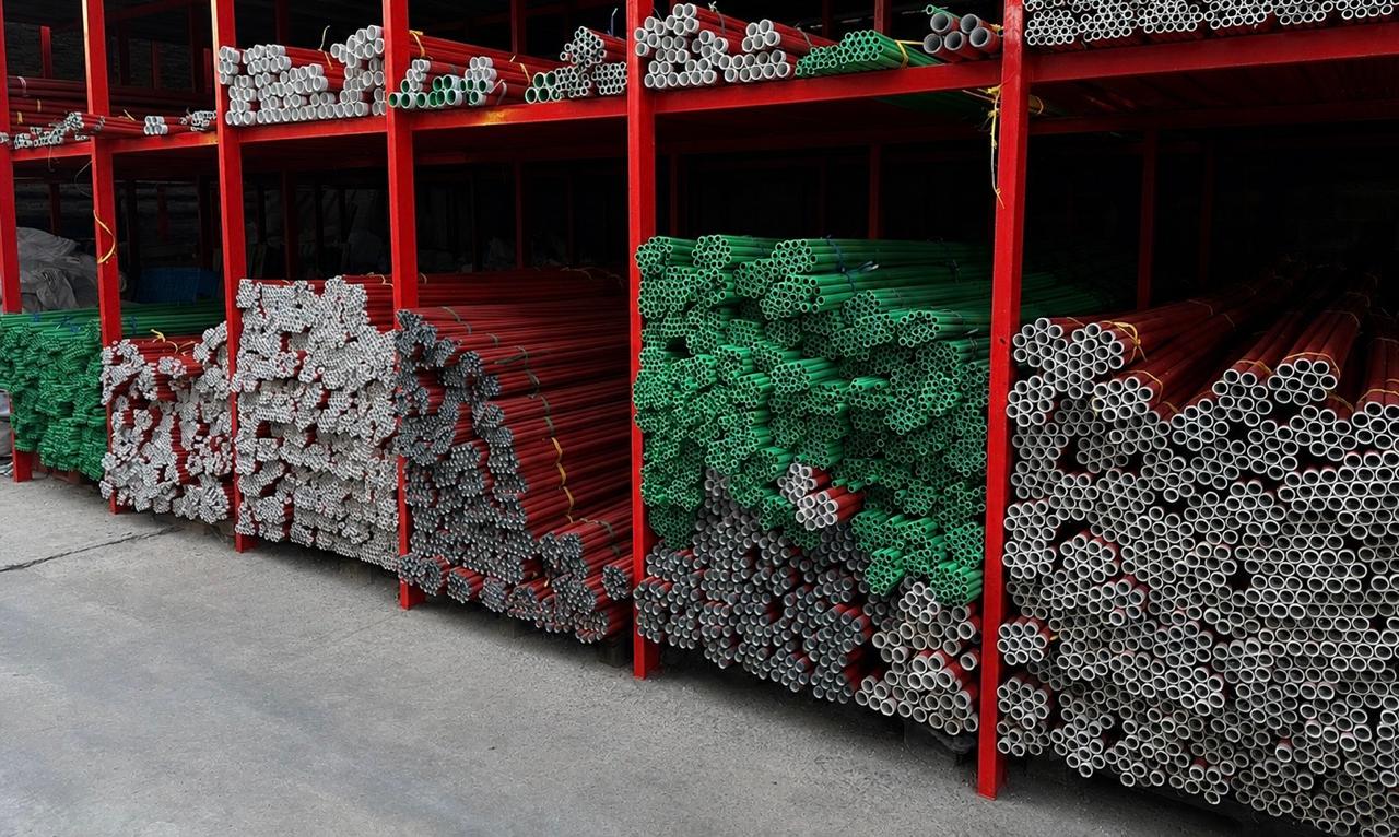 Estanterías con stock de tubos de polipropileno rojos, verdes y grises en la fábrica IGUADUC